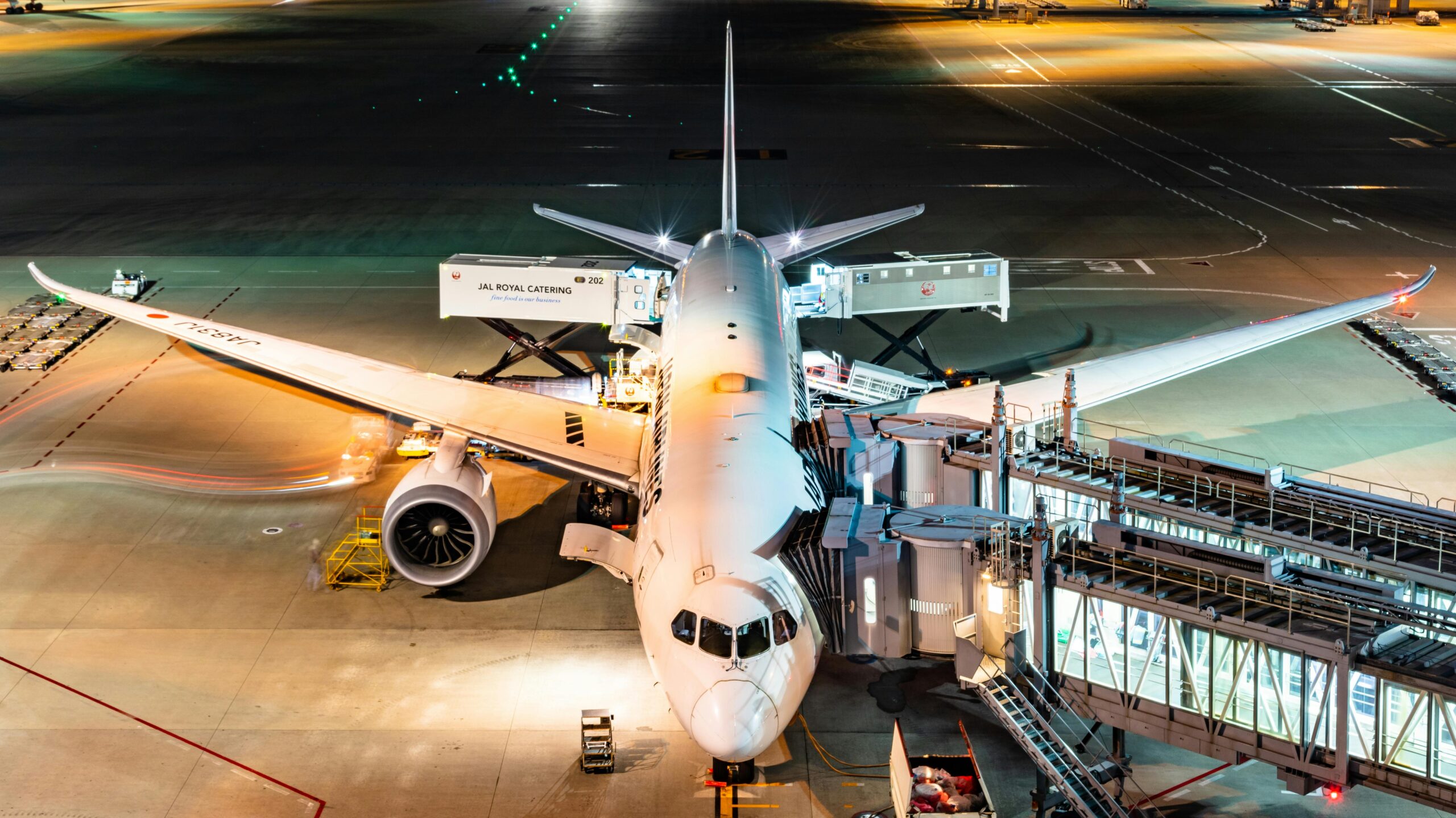 Aerial view of an Airbus being boarded at night in Tokyo's bustling airport.